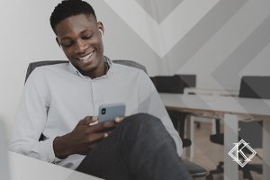 A imagem mostra um homem sorrindo e lendo algo no celular. Ilustra a publicação 