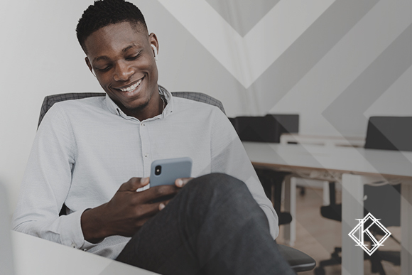 A imagem mostra um homem sorrindo e lendo algo no celular. Ilustra a publicação "Contrato de Trabalho no Exterior: o que devo saber?", da Koetz Advocacia.