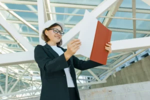 A imagem mostra uma mulher arquiteta, com capacete de obras, analisando documentos. Ilustra o texto sobre empregos para estrangeiros no Brasil.