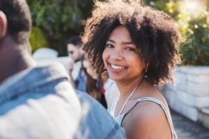 A imagem mostra uma jovem mulher sorrindo, olhando para a câmera, ao ar livre. Ilustra o texto sobre quando um imigrante tem direito de permanecer no Brasil.