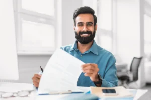 A imagem mostra um jovem homem, sorrindo para a câmera, enquanto mexe em documentos. Ilustra o texto sobre Apostilamento de documentos.