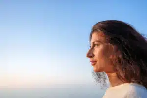 A imagem mostra uma jovem mulher pensativa, de perfil, olhando para o pôr do sol. Ilustra o texto sobre refugiados no Brasil.