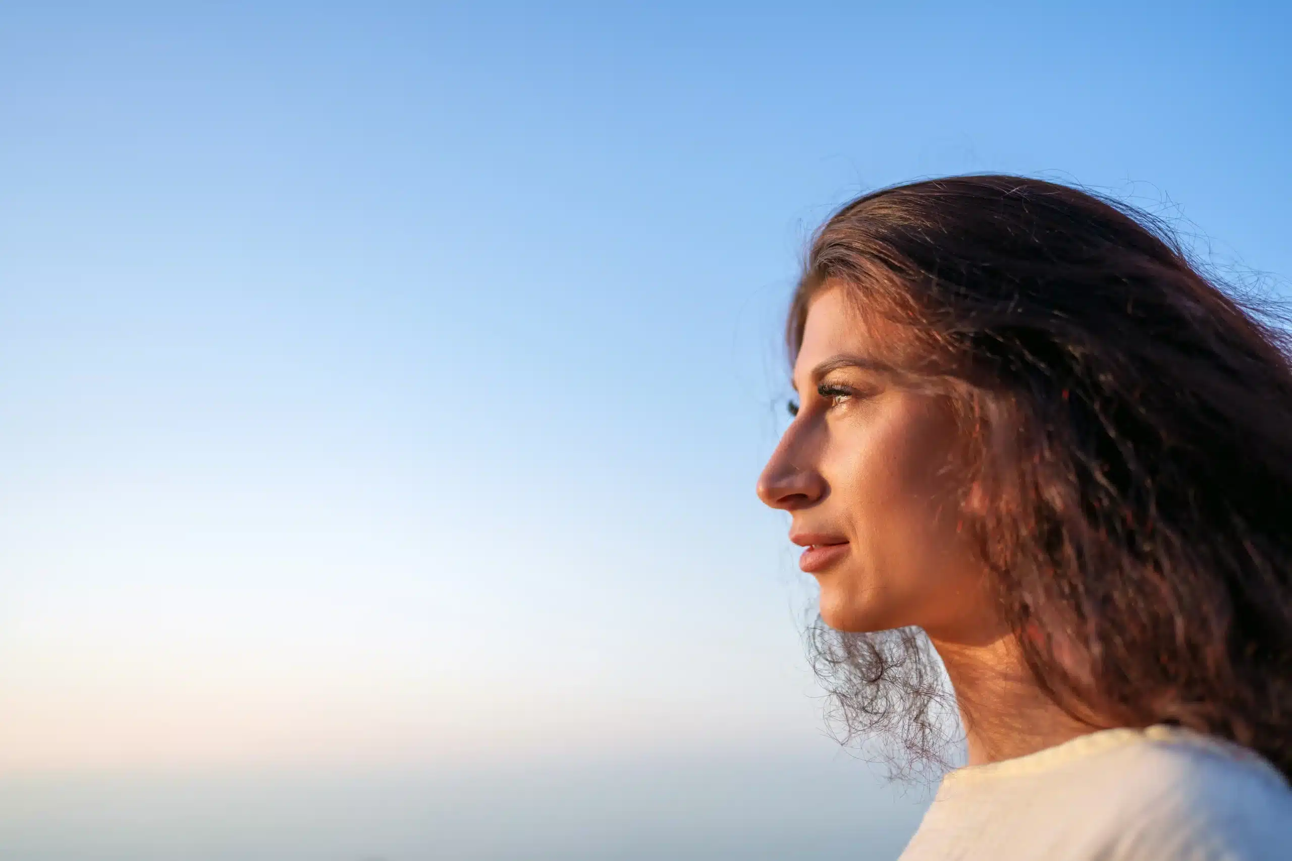 A imagem mostra uma jovem mulher pensativa, de perfil, olhando para o pôr do sol. Ilustra o texto sobre refugiados no Brasil.