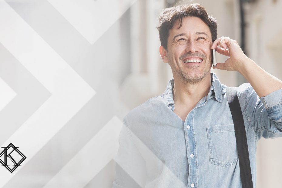 A imagem mostra um homem sorrindo e caminhando na rua enquanto atende o telefone, e ilustra a publicação "Imigrante que comprar imóvel pode ter autorização de residência brasileira", da Koetz Advocacia.