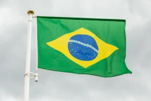 A imagem mostra a bandeira do Brasil, balançando contra o vento. Ilustra o texto sobre Embaixadas e Consulados no Brasil.