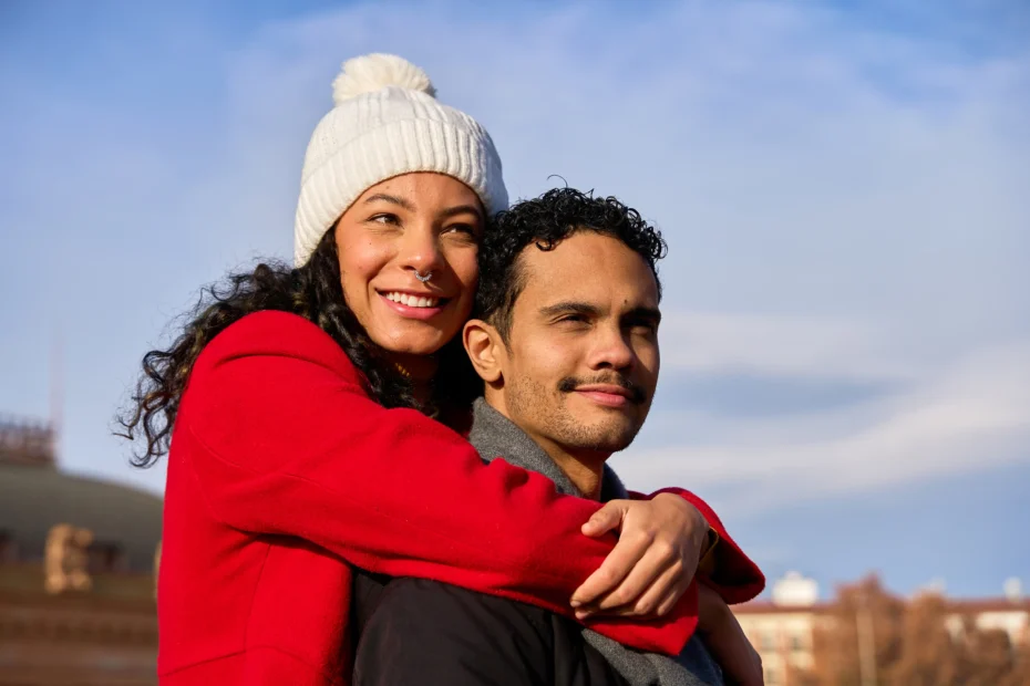 A imagem mostra um casal latino feliz se abraçando ao ar livre em roupas de inverno. Ilustra o texto sobre autorização de residência.