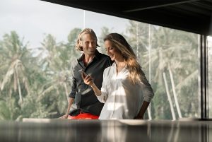 A imagem mostra um homem e uma mulher juntos, enquanto a mulher olha para o celular que está segurando e o homem sorri para ela e ilustra o texto: Brazilian residence permit for foreigners who buy property da Koetz Advocacia.