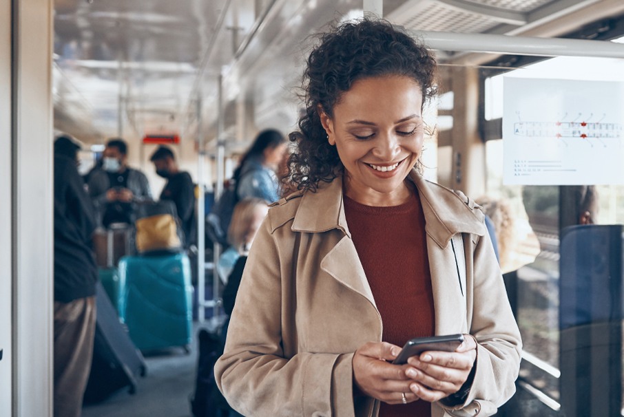 A imagem mostra mulher em um ônibus sorrindo enquanto olha para seu celular