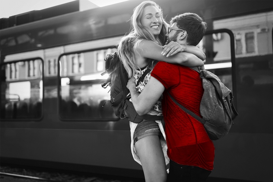 A imagem mostra um casal jovem se abraçando em uma estação de trem