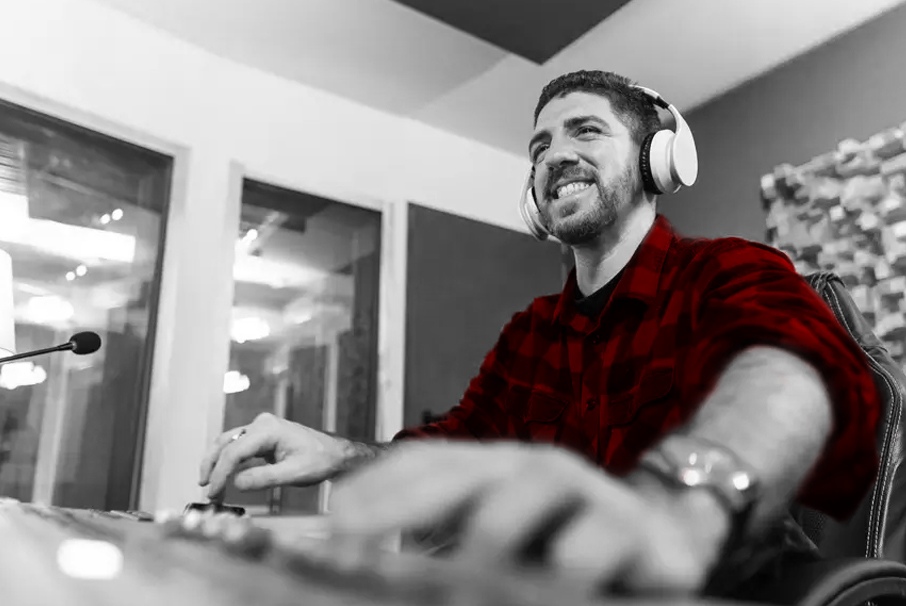 A imagem mostra um homem sorridente em um estúdio, em seu computador