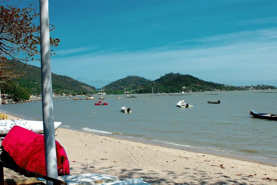 A imagem mostra a praia de Florianópolis, com vários barcos no mar. A imagem ilustra o texto 