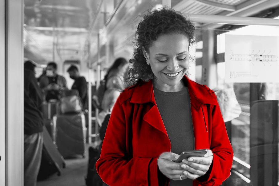 A imagem mostra mulher em um ônibus sorrindo enquanto olha para seu celular