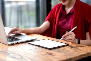 A imagem mostra uma mulher usando o notebook e o tablet, sentada em uma cadeira e ilustra o texto: Tax Resident and Non-Resident da Koetz Advocacia.