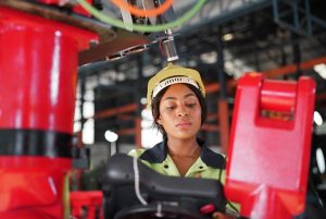 A imagem mostra uma mulher adulta trabalhando como engenheira robótica em uma fábrica. A imagem ilustra o texto 