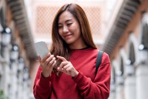 A imagem mostra uma jovem mulher sorrindo enquanto olha para a tela de seu celular. Imagem ilustrando o texto 