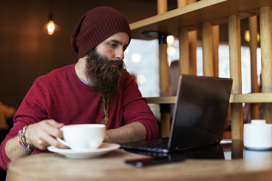 A imagem mostra um homem em um café, segurando uma xícara, enquanto olha para um notebook e ilustra o texto: Online divorce: how does it work? da Koetz Advocacia.