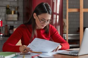 The image shows a woman looking at the various papers and pens around her. ilustrating the article 