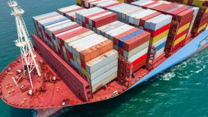 A imagem mostra uma visão aérea de mar, em especial de um navio carregado de containers e ilustra o texto: Contratos internacionais de exportação do Brasil para exterior da Koetz Advocacia.