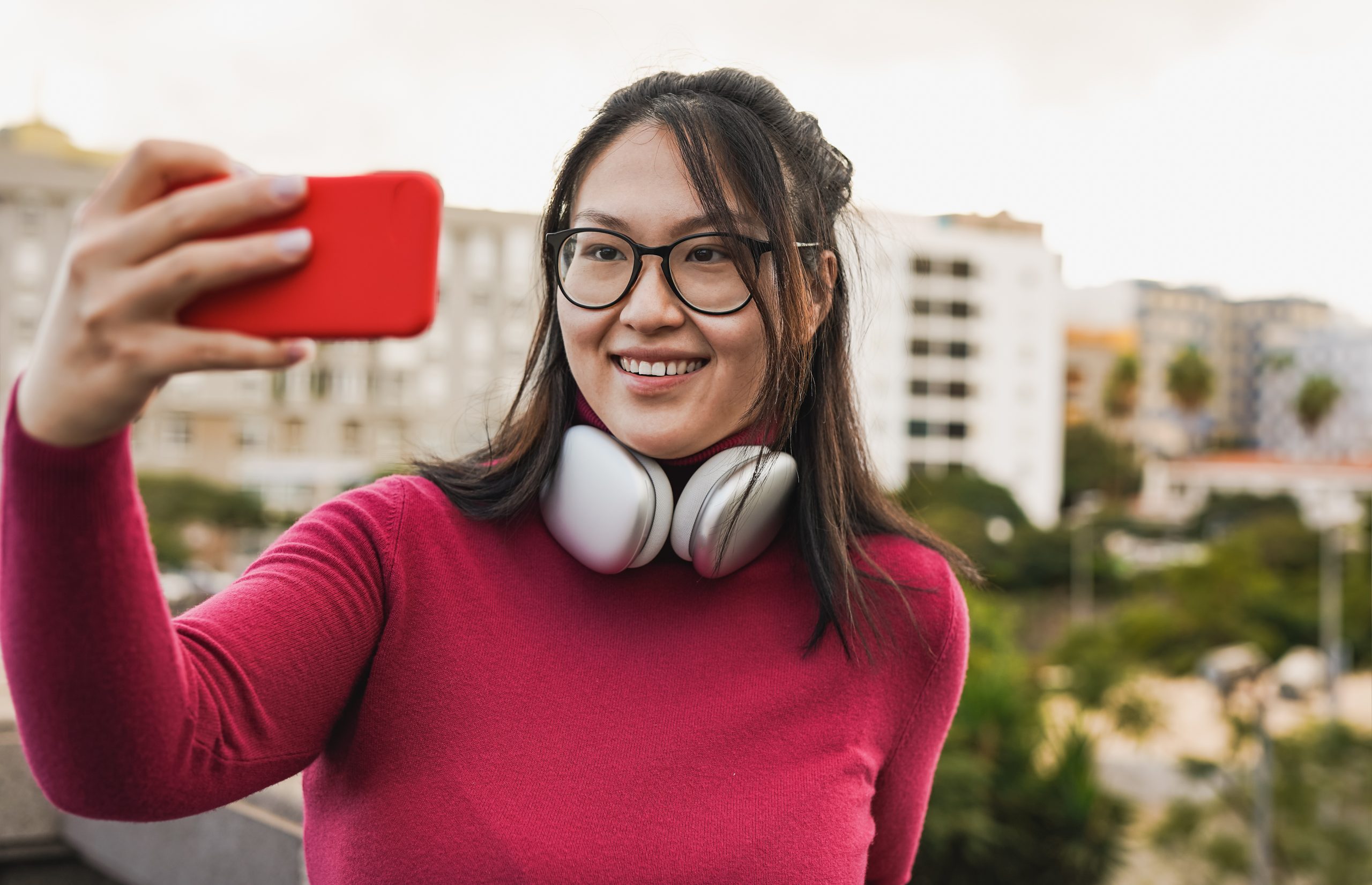 A imagem mostra uma mulher sorrindo, enquanto posa para uma selfie e usa fones de ouvido, ao ar livre e ilustra o texto: Como Revalidar e Reconhecer Diplomas Estrangeiros no Brasil da Koetz Advocacia.