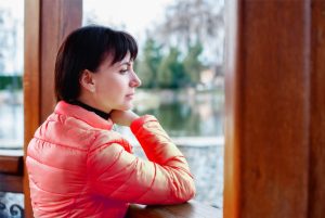 La imagen muestra a una mujer con mirada triste mirando por la ventana y ilustrando el articulo Pensión brasileña para viudo o viuda de extranjero de Koetz Advocacia.