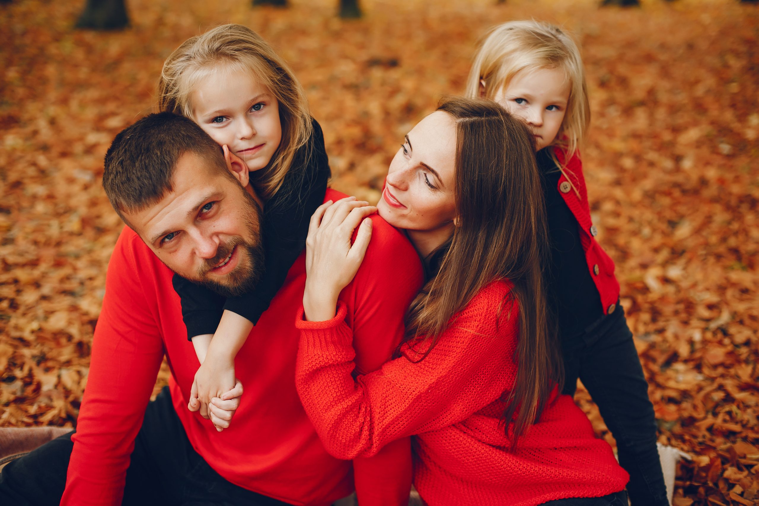 A imagem mostra uma família: pai, mãe e 2 filhas crianças, em um parque ao ar livre, enquanto os 4 se abraçam e ilustra o texto: Vantagens da Sucessão Familiar no Brasil – comparativo com Portugal da Koetz Advocacia.