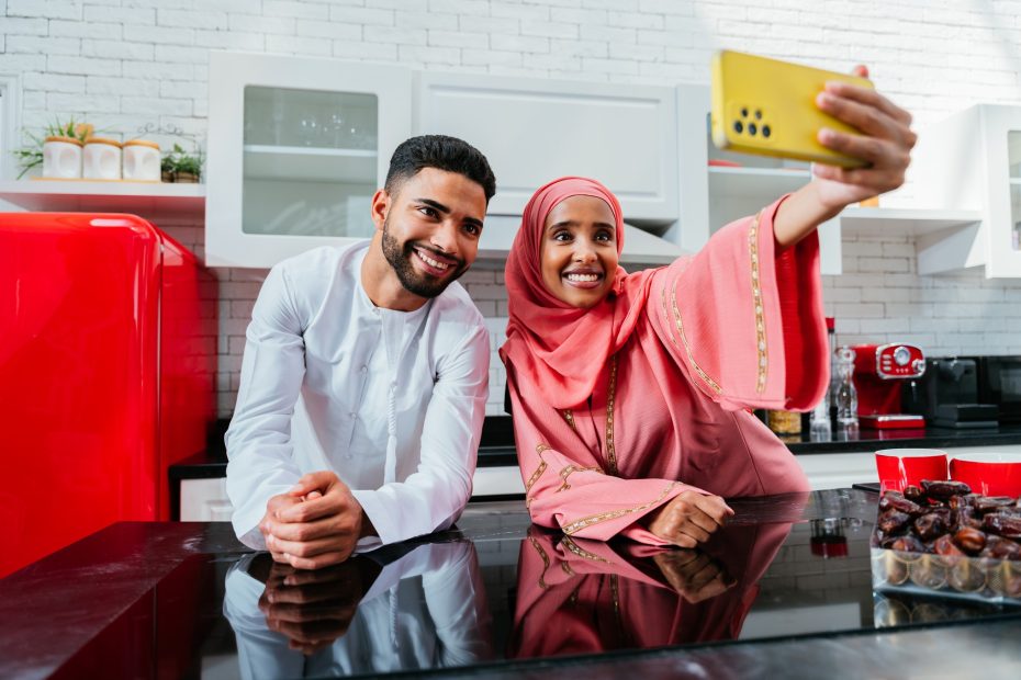 A imagem mostra um casal feliz, sorrindo, do Oriente Médio, em trajes tradicionais, em uma cozinha e tirando uma selfie e ilustra o texto: Arab marriage: differences, religions, and characteristics of each arab country da Koetz Advocacia.