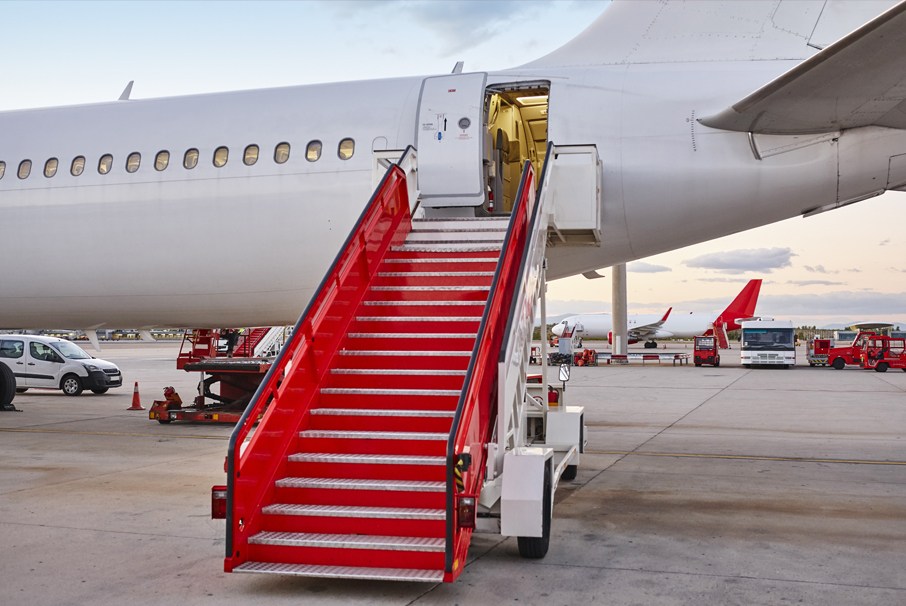 A imagem mostra um aeroporto com avião e escadas. A imagem ilustra o texto "Visto brasileiro para tripulação de aeronaves" de Koetz Advocacia