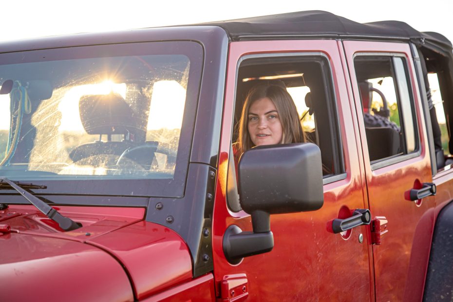 A imagem mostra uma jovem mulher dirigindo um carro em uma área de campo e ilustra o texto National Driver's License for Foreigners in Brazil da Koetz Advocacia.