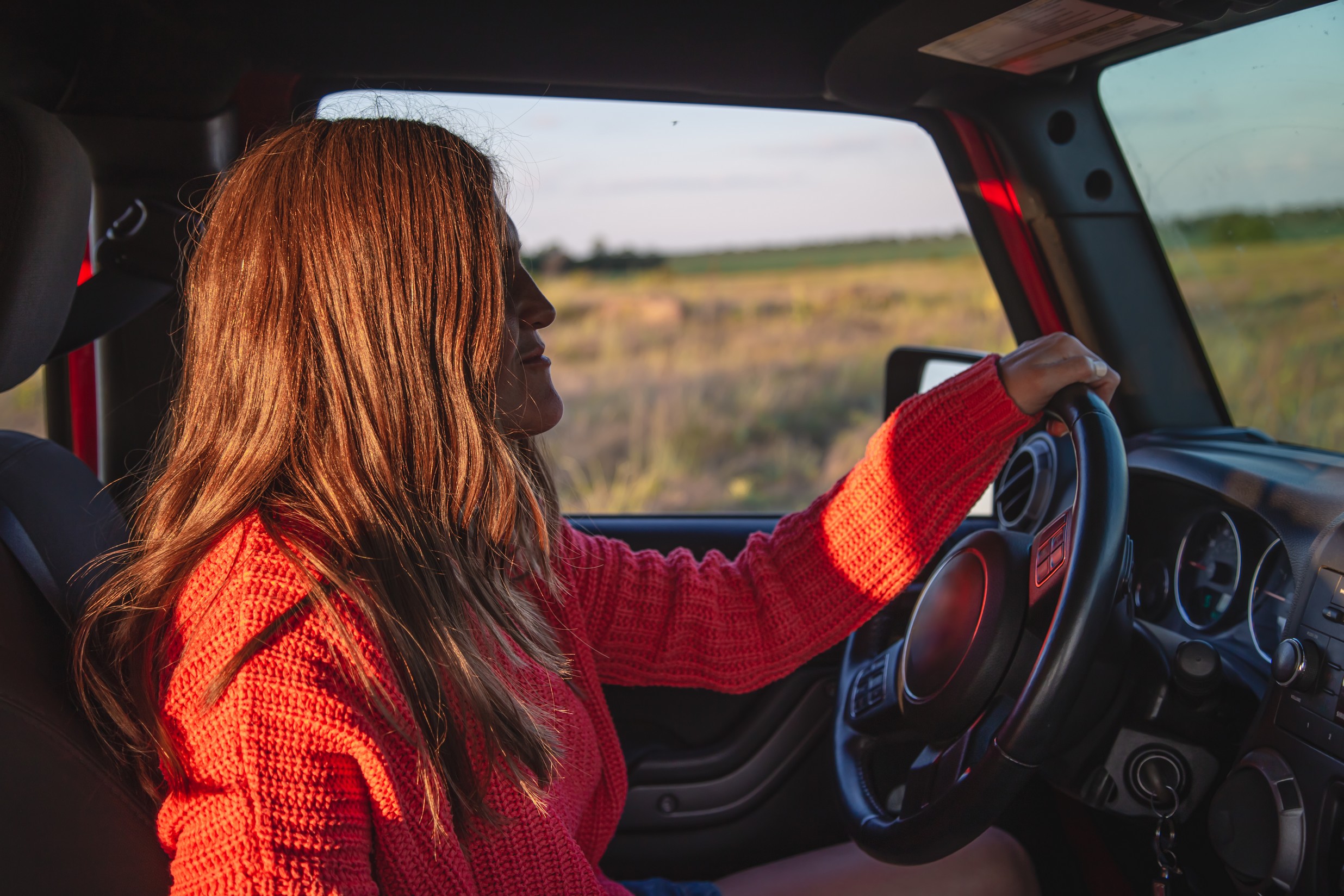 A imagem mostra uma jovem mulher dirigindo um carro, no campo e ilustra o texto: Carteira Nacional de Habilitação para Estrangeiros no Brasil da Koetz Advocacia.