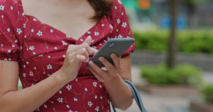 A imagem mostra uma mulher usando um smartphone ao ar livre e ilustra o texto: Importação de Iphone: o que você precisa saber da Koetz Advocacia.