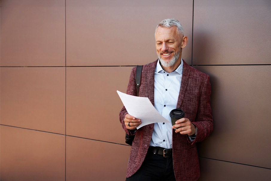 The image shows a mature man smiling while looking at papers. ilustrating the article "What are the types of Naturalization for foreigners in Brazil?" Koetz Advocacia.