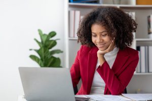 A imagem mostra uma jovem mulher sorrindo, enquanto usa um laptop e ilustra o texto: Guia do Investimento Estrangeiro em startup da Koetz Advocacia.