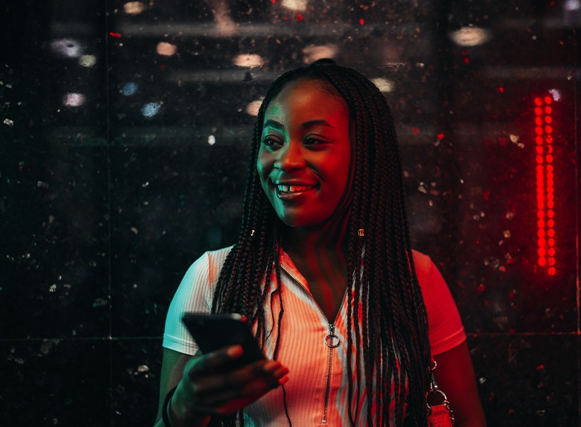 The image shows a young and cheerful woman using her cell phone on the subway at night. ilustrating the article "How to obtain Brazilian naturalization: all you need to know" Koetz Advocacia.