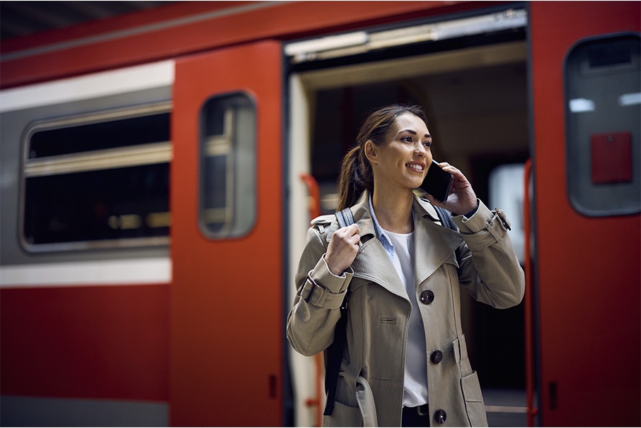 The image shows a happy woman talking on her cell phone at the train station, illustrating the article "Migratory Year: how does it affect your trip or move to Brazil?" Koetz Advocacia