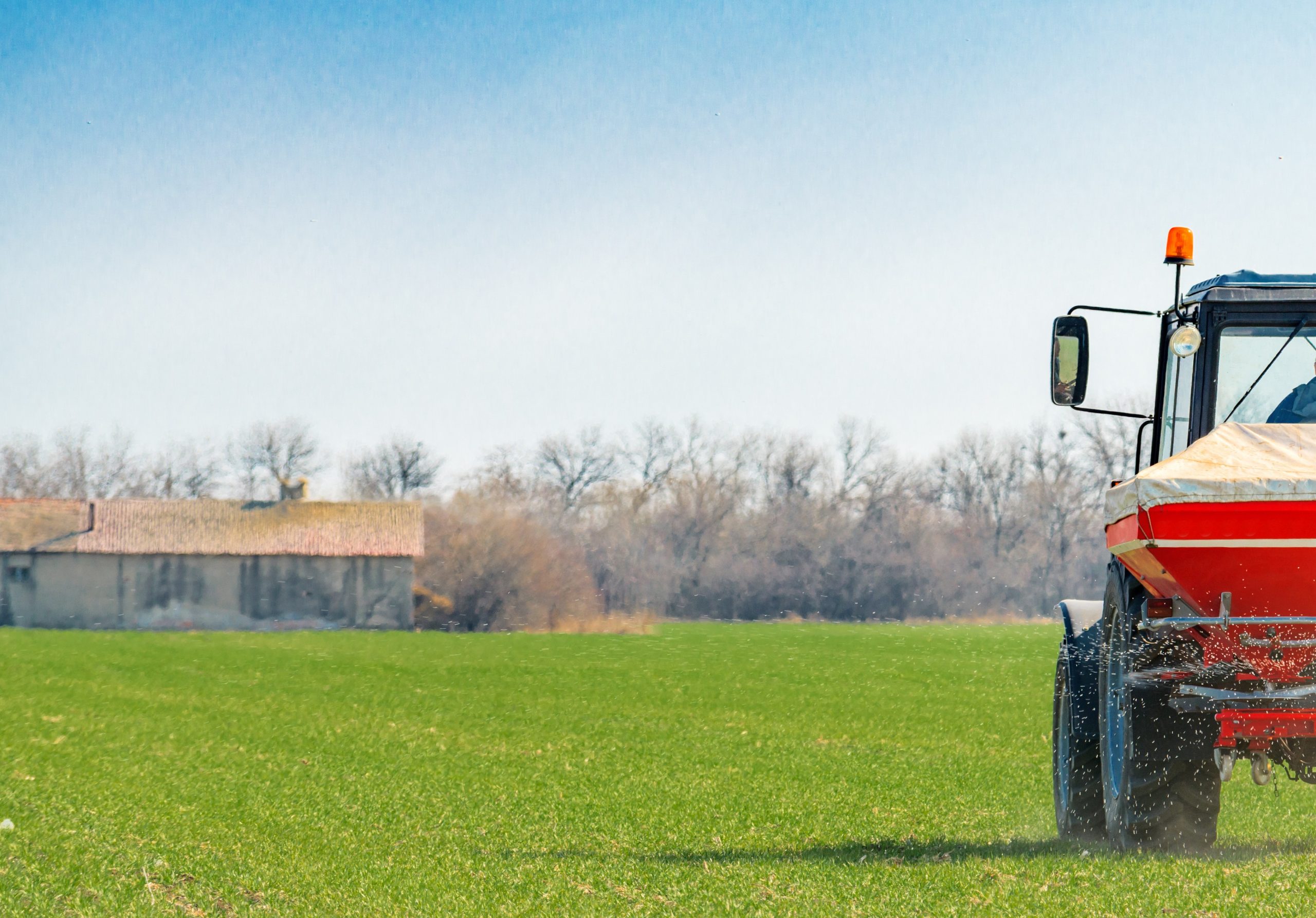 A imagem mostra um trator agrícola fertilizando um campo de trigo e ilustra o texto: Importing Fertilizers: what you should know da Koetz Advocacia.