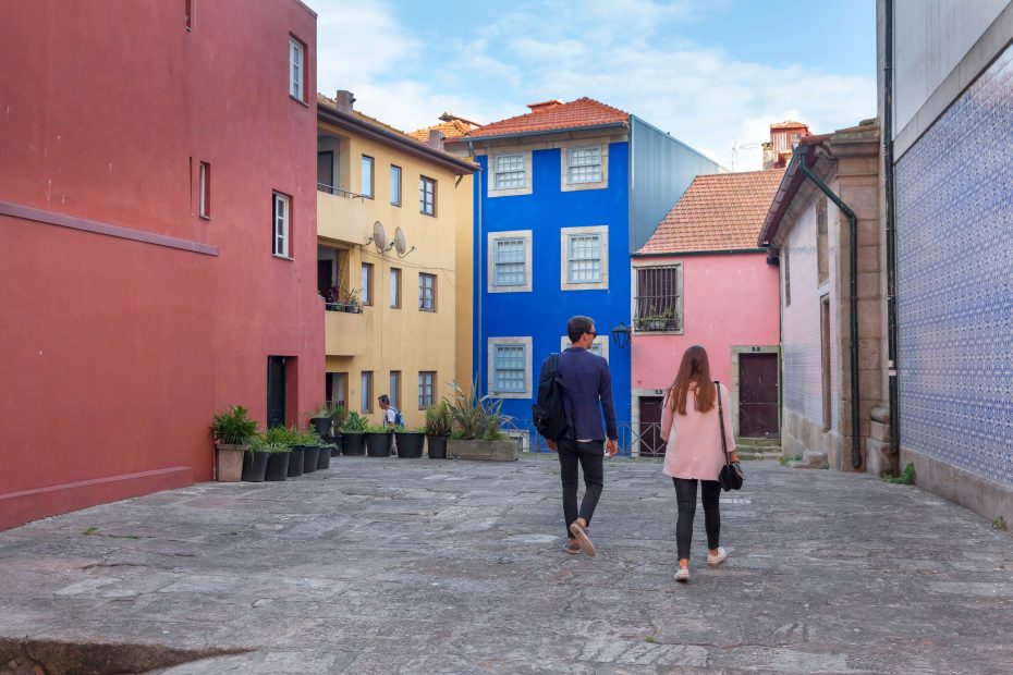 A imagem mostra um casal andando em uma rua colorida, em Porto, Portugal e ilustra o texto: Guia do Visto CPLP para Portugal da Koetz Advocacia.