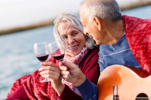 A imagem mostra um casal sênio feliz, brindando com taças de vinho, enquanto aproveita o momento juntos e ilustra o texto: Brazilian Retirement Visa: where should I pay income tax? da Koetz Advocacia.