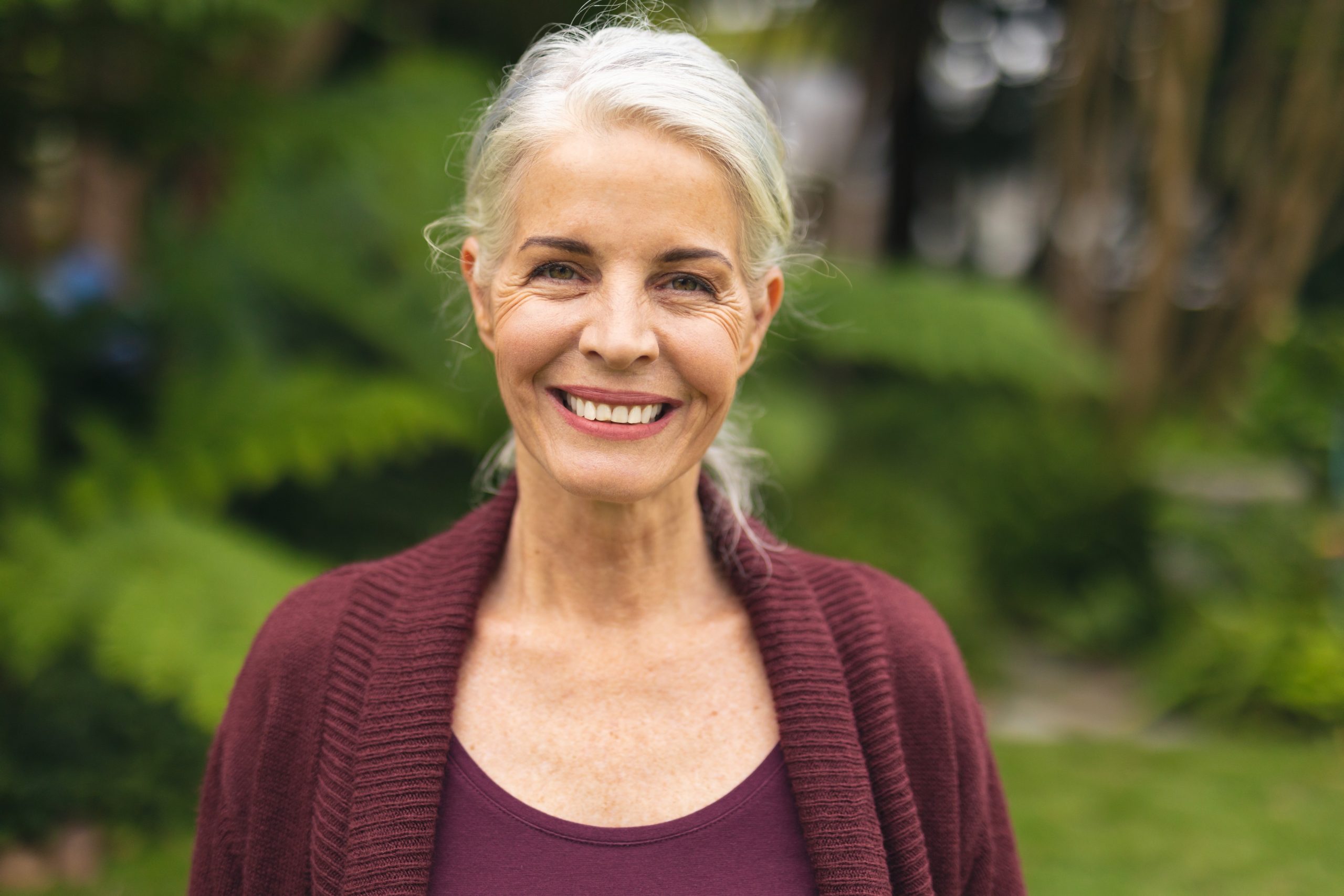 A imagem mostra uma mulher sênior caucasiana, sorrindo para a câmera, ao ar livre e ilustra o texto: Visto de aposentado brasileiro: onde devo pagar imposto de renda? da Koetz Advocacia.