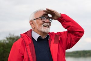 A imagem mostra um homem sênior, usando óculos, sorrindo, enquanto está em meio à natureza e ilustra o texto: Visto D7 para Portugal: o que é? da Koetz Advocacia.