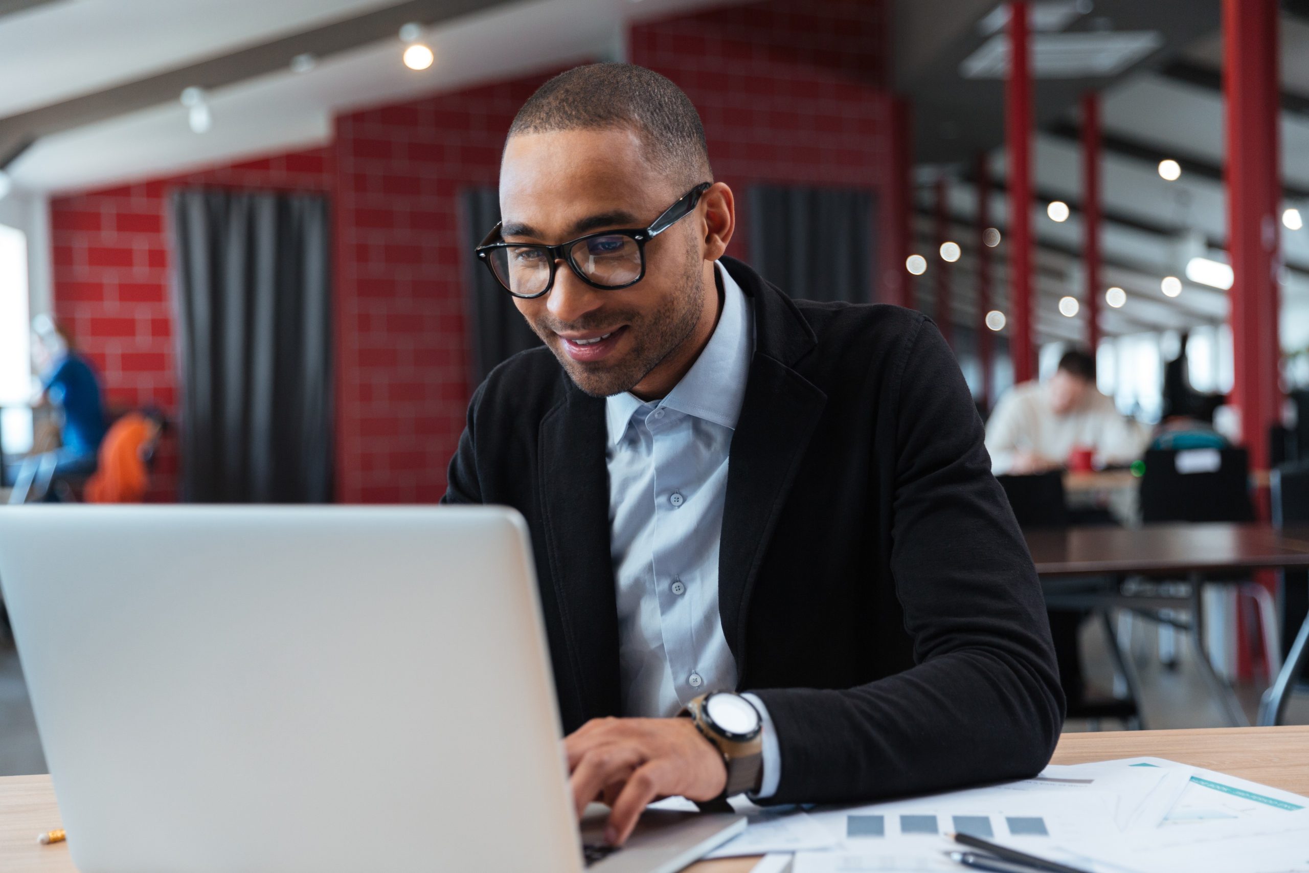 A imagem mostra um jovem homem de negócios, de terno e gravata, trabalhando em seu laptop enquanto dá um leve sorriso e ilustra o texto: Convertible Loan: Advantages of the format in Foreign Investment da Koetz Advocacia.