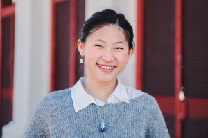 The image shows a young Asian woman smiling at the camera and illustrates the text: How can a foreigner live in Brazil? from Koetz Advocacia.