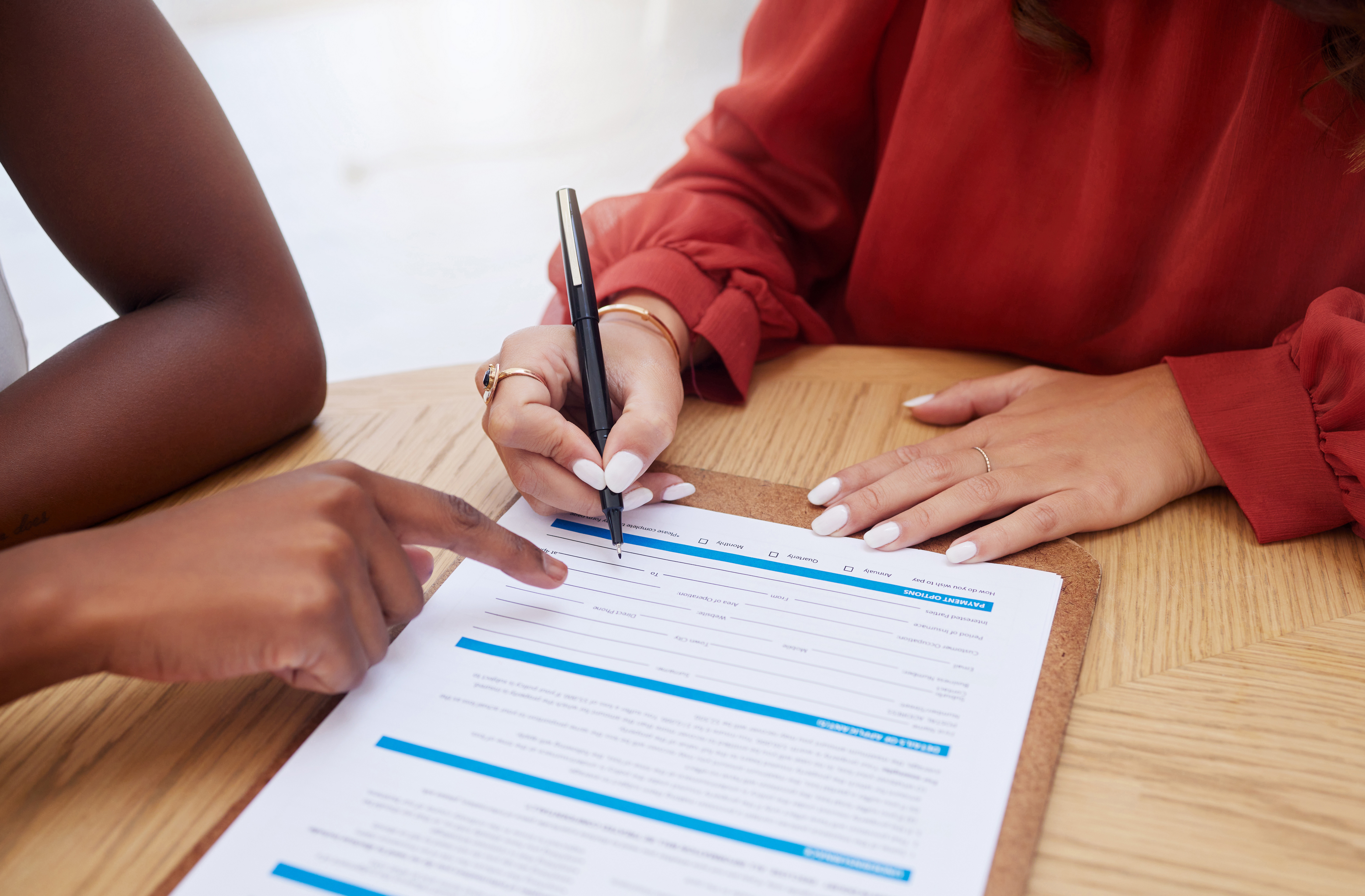 A imagem mostra em um close-up duas mulheres assinando um contrato, enquanto uma aponta para o papel e a outra segura uma caneta com uma das mãos e ilustra o texto: Hiring a foreigner in Brazil da Koetz Advocacia.