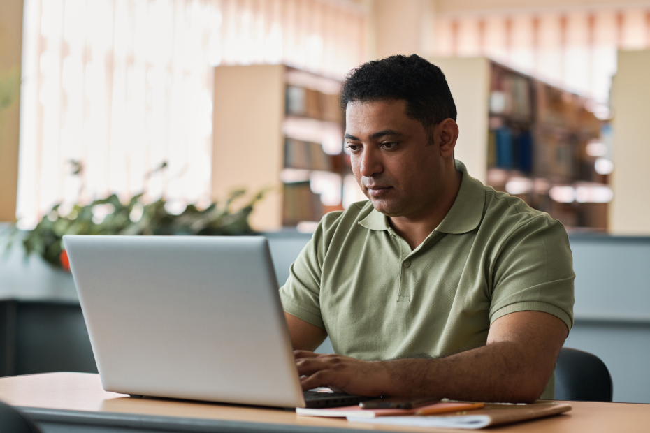 A imagem mostra um homem, sentado em uma cadeira, com os braços apoiados em uma mesa, enquanto usa o laptop e ilustra o texto: Tarjeta Nacional de Registro de Migración: ¿qué es y cómo obtenerla? da Koetz Advocacia.