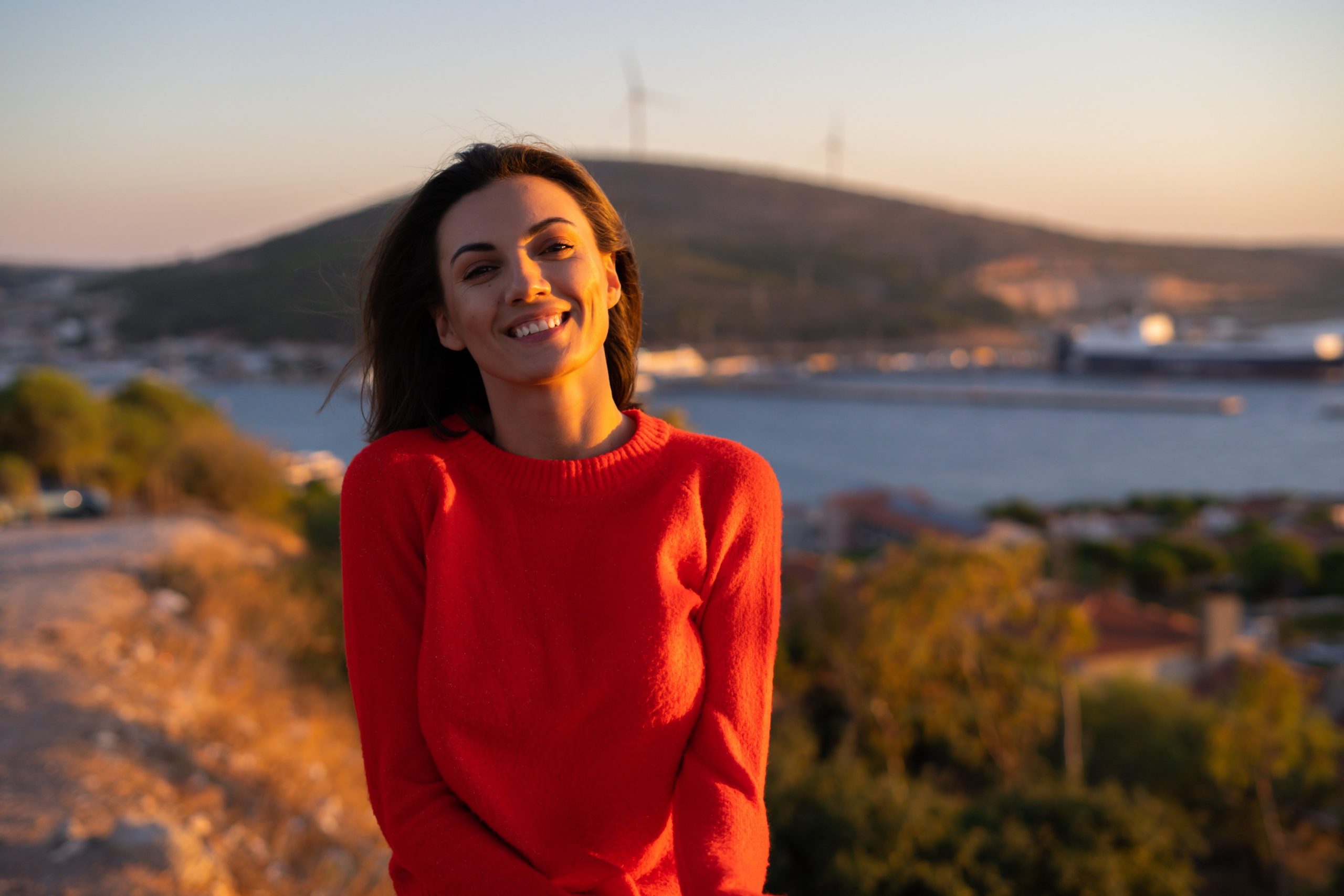 A imagem mostra uma jovem mulher, com suéter, ao ar livre, sorrindo e olhando para a câmera e ilustra o texto: CPLP: Concessão de vistos e autorização de residência mais fácil para estrangeiros e brasileiros da Koetz Advocacia.