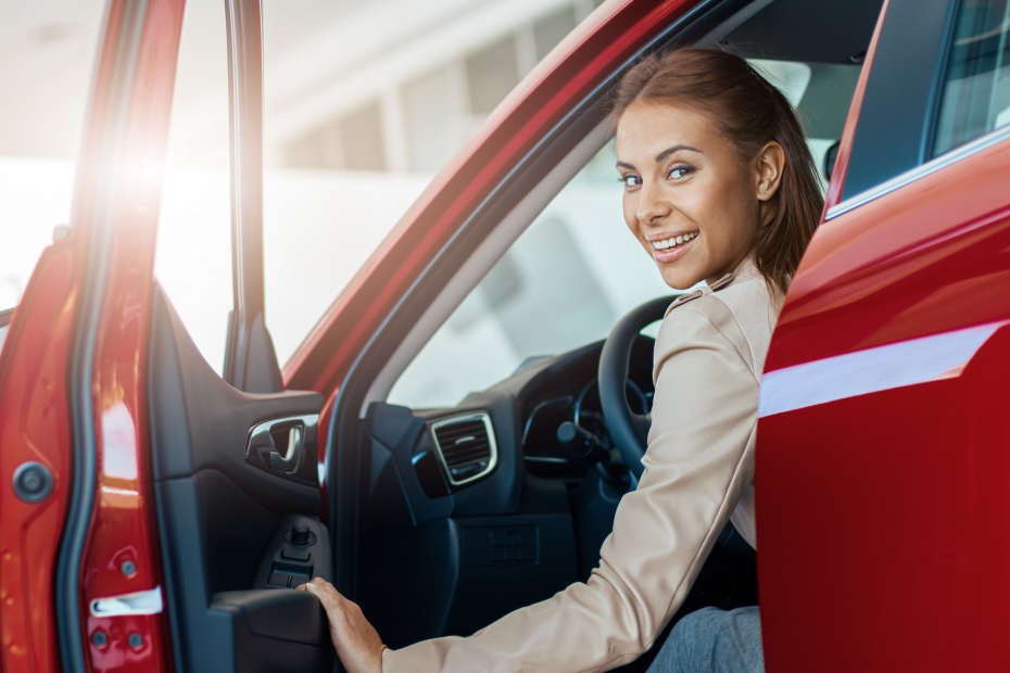 A imagem mostra uma jovem mulher sorrindo, dentro de seu carro, no banco do motorista e ilustra o texto: Import and export of own vehicles da Koetz Advocacia.