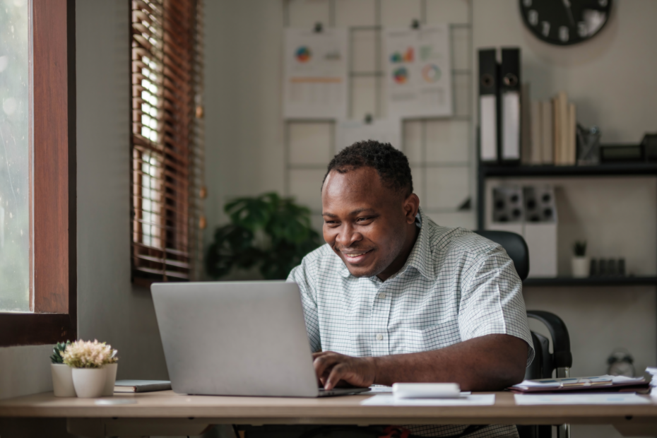 A imagem mostra um homem negro sorridente, usando o laptop em casa e ilustra o texto: Moradia no Brasil: Como funciona? Um guia para imigrantes da Koetz Advocacia.