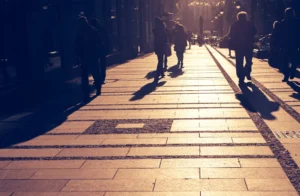 A imagem mostra silhuetas de pessoas andando em uma rua. A imagem ilustra o texto 