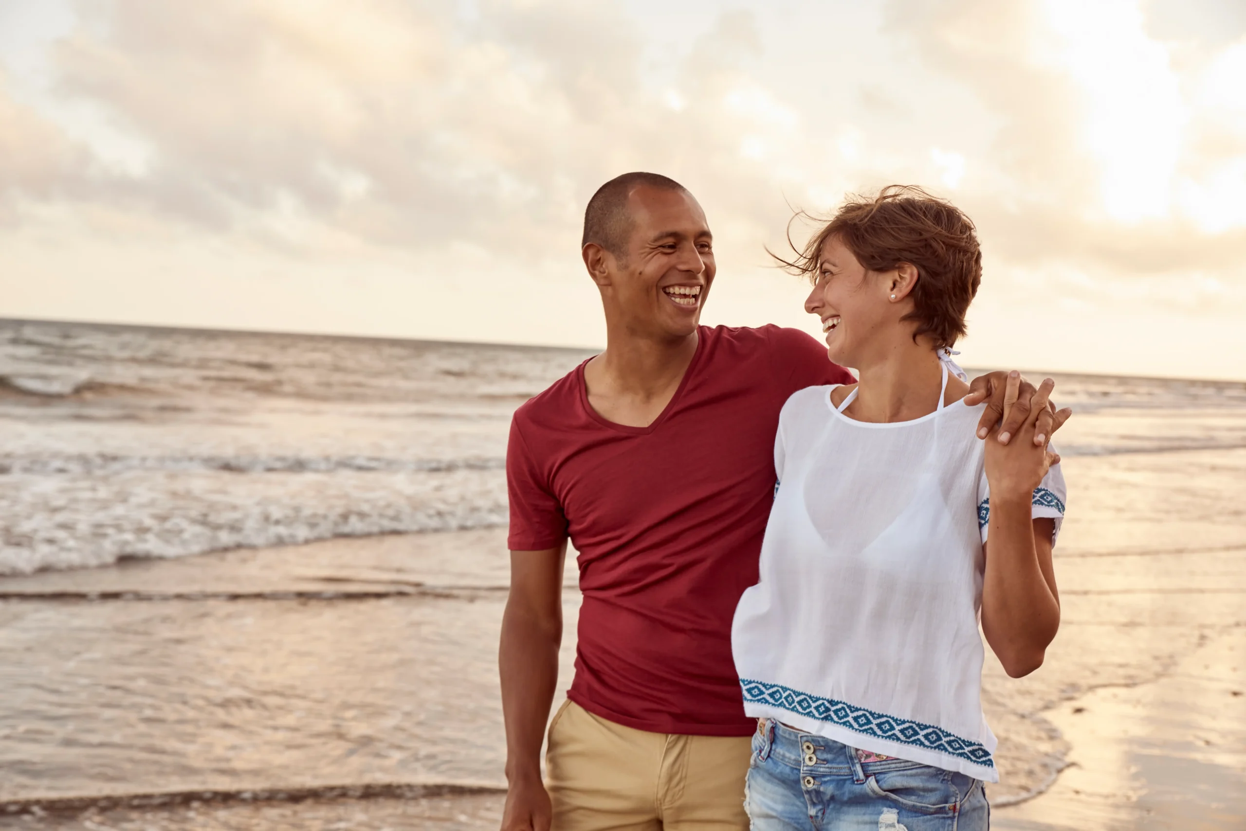 A imagem mostra um casal feliz, lado a lado, andando pela praia.