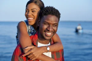 A imagem mostra um casal juntos, sorrindo, ao ar livre, na praia.