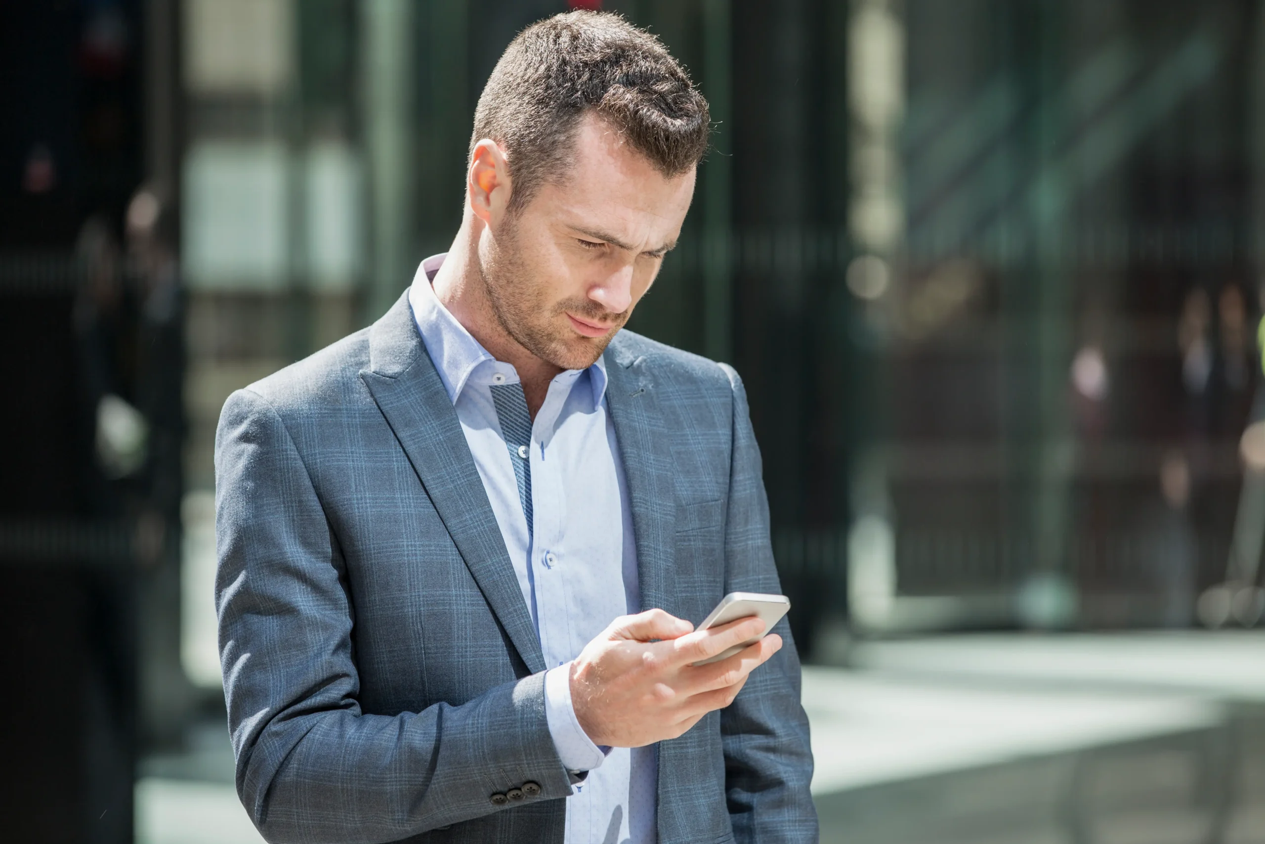 La imagen muestra a un empresario, interesado en una visa de inversionista, usando un teléfono celular. Tiene el pelo castaño corto y viste un traje azul.